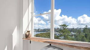 Una habitación con un ventanal grande, una estantería de madera, un banco y un florero.