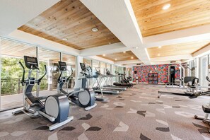 Ein Fitnessraum mit Laufbändern, Ergometer und Crosstrainern, großen Fenstern und einer farbenfrohen Wand.