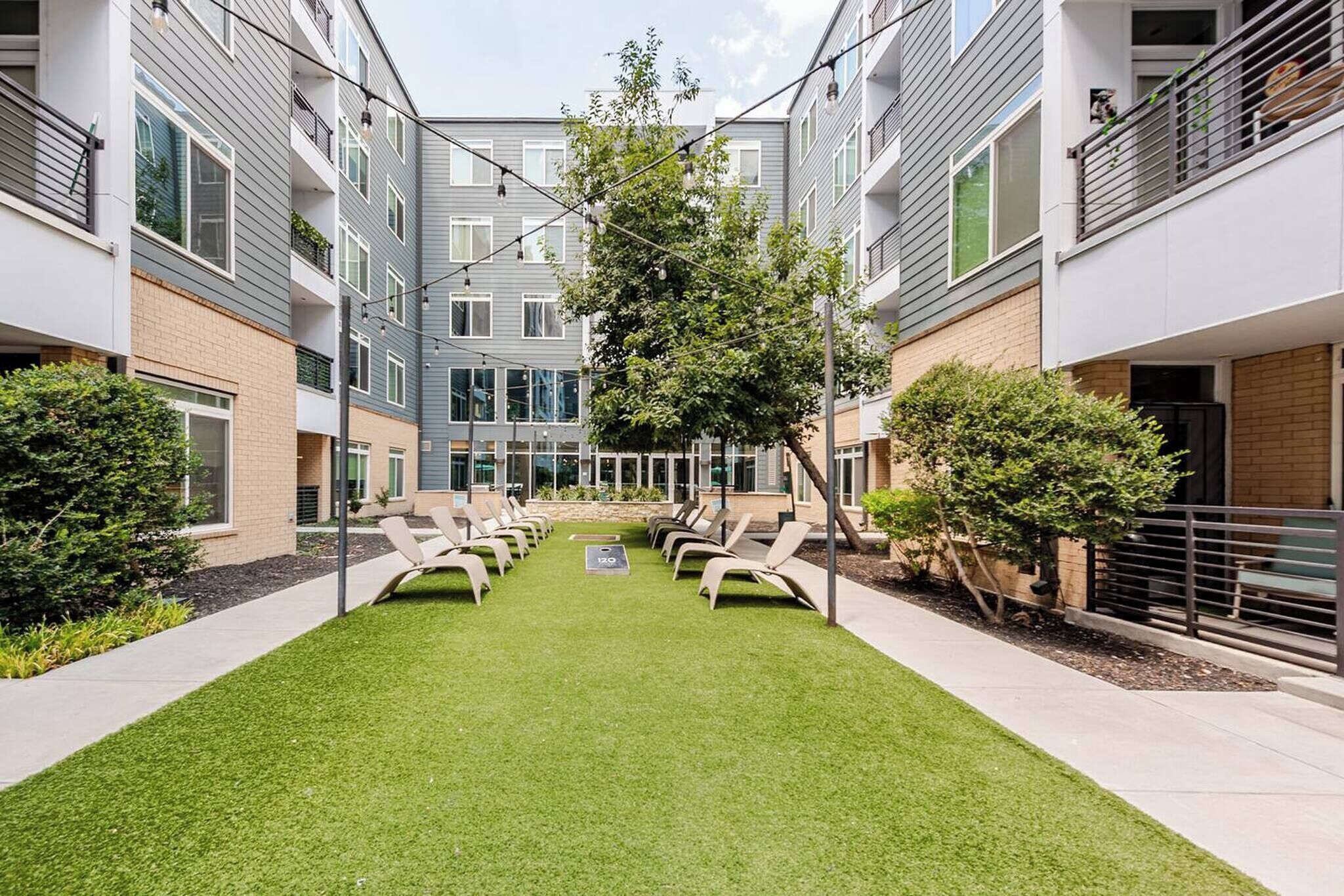 A courtyard with a green lawn, lounge chairs, and a central tree.
