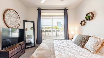Un dormitorio con cama, televisión, cómoda, espejo y vista al balcón.