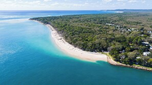 An aerial view of a coastal area with a beach, dense forest, and scattered buildings. - Amity Treetops - beautiful coastal escape (Amity)