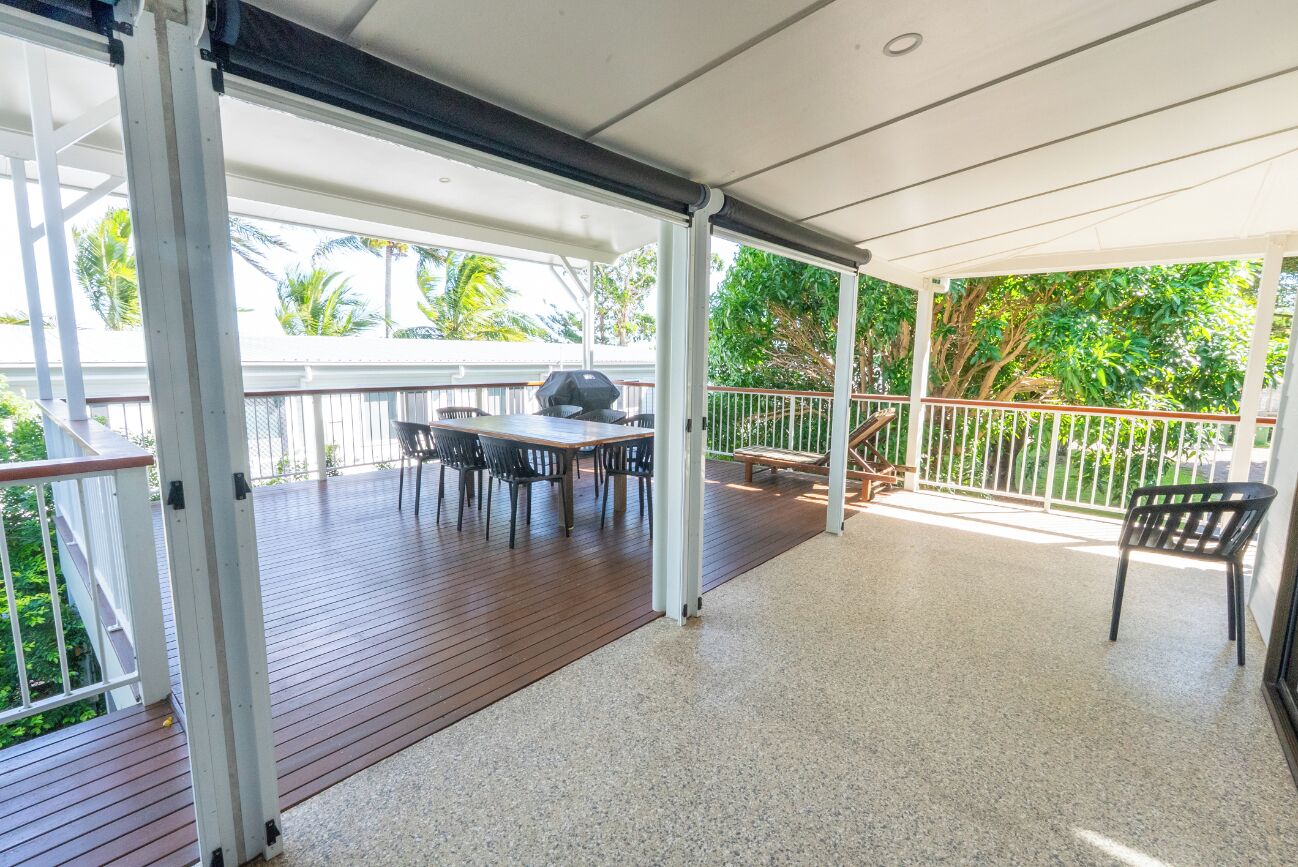 A covered outdoor area with a wooden deck, a table with chairs, and a grill.