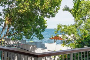 A view of the ocean from a balcony with a wooden railing, surrounded by lush green foliage and a small wooden structure. - Amity Treetops - beautiful coastal escape (Amity)