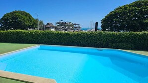 Una piscina blava i transparent amb vista a un edifici i arbres al fons.
