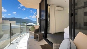 Een balkon met glazen hekwerk, een bank en een stoel, met uitzicht op een bergachtig landschap.