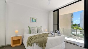 Een moderne slaapkamer met een groot bed, een nachtkastje, een raam met uitzicht op gebouwen en een plafondventilator.