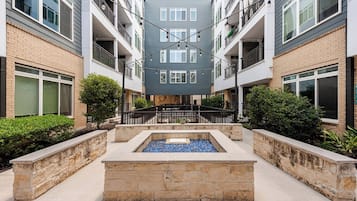 A multi-story residential building with balconies, a central courtyard with a water feature, and a stone retaining wall.