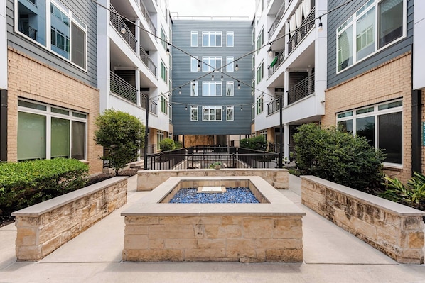 A multi-story residential building with balconies, a central courtyard with a water feature, and a stone retaining wall. - Riverwalk & Pool View Condo Pets & Free Parking (San Antonio)