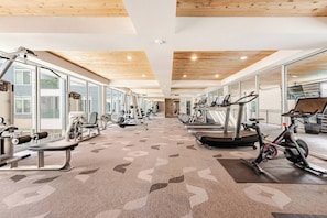 Une salle de sport équipée de matériel d’exercice, dotée de grandes fenêtres et recouverte d’un tapis à motifs.