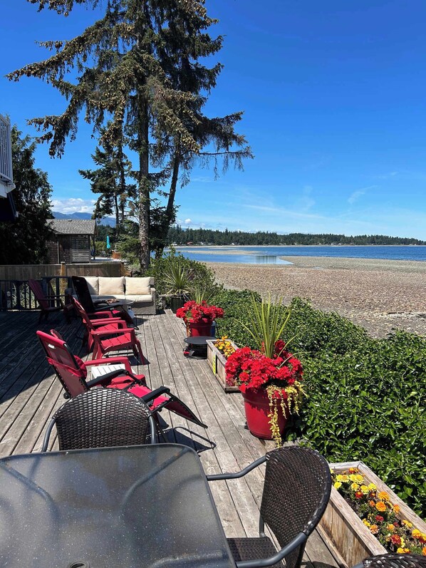 A deck with outdoor furniture, a view of the beach, and a forested area. - Seaside Pines Escape (Qualicum Beach)