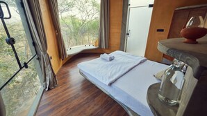A bedroom with a wooden floor, a bed with white linens, a window with curtains, and a wooden cabinet with a glass bottle. - Winterfell by Sanctity Ferme Stays (Shoolagiri)