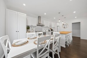 Una cocina moderna con armarios blancos, una isla central y un comedor con sillas blancas y una mesa de madera.