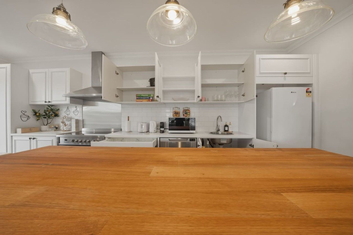 Una cucina moderna con mobili bianchi, un tavolo da pranzo in legno e illuminazione a sospensione.