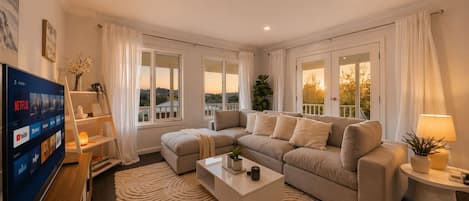 A modern living room with a sectional sofa, a flat-screen TV, and a large window with curtains.