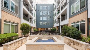A multi-story residential building with balconies, a central courtyard with a water feature, and surrounding greenery. - Luxury Riverwalk Penthouse Pool & Skyline Views (San Antonio)