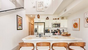 A modern kitchen with white cabinetry, a central island with bar stools, stainless steel appliances, and decorative wall art. - Luxury Riverwalk Penthouse Pool & Skyline Views (San Antonio)