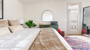 A bedroom with a bed, a mirror, a desk, a plant, and a door leading to a balcony. - Luxury Riverwalk Penthouse Pool & Skyline Views (San Antonio)