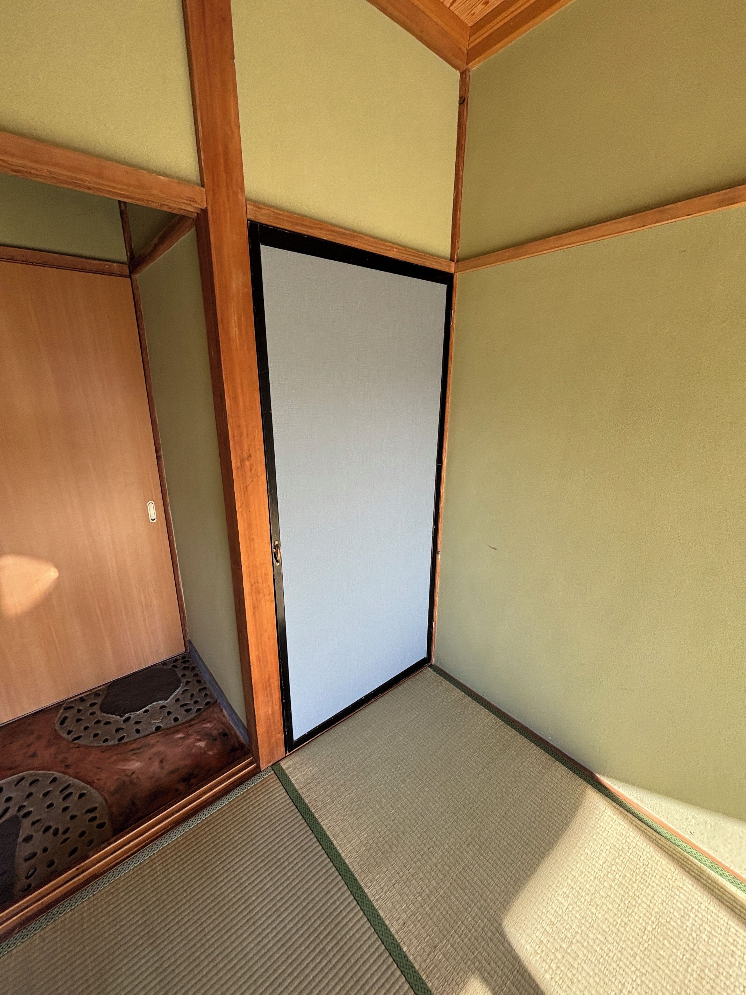 Una stanza con pavimento in tatami, una porta in legno e un piccolo spazio contenitore.