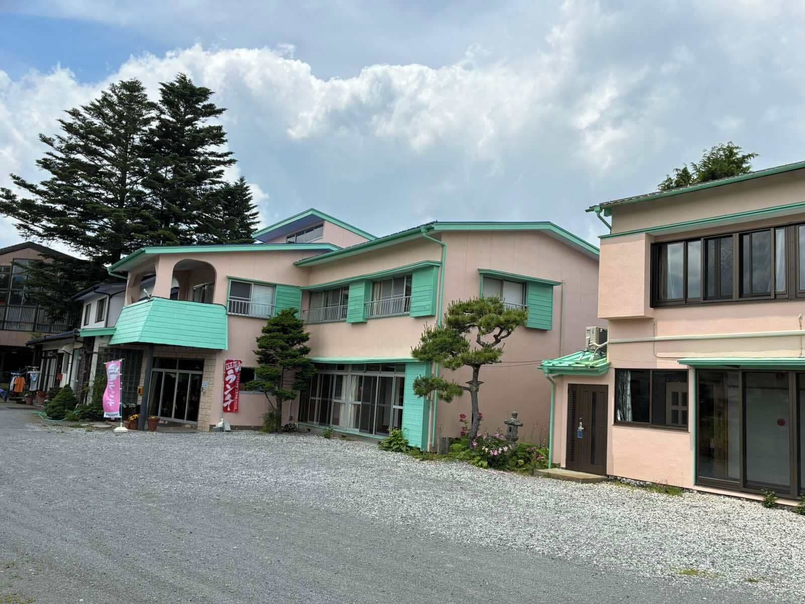 A building with a green roof, a large tree, and a gravel driveway.