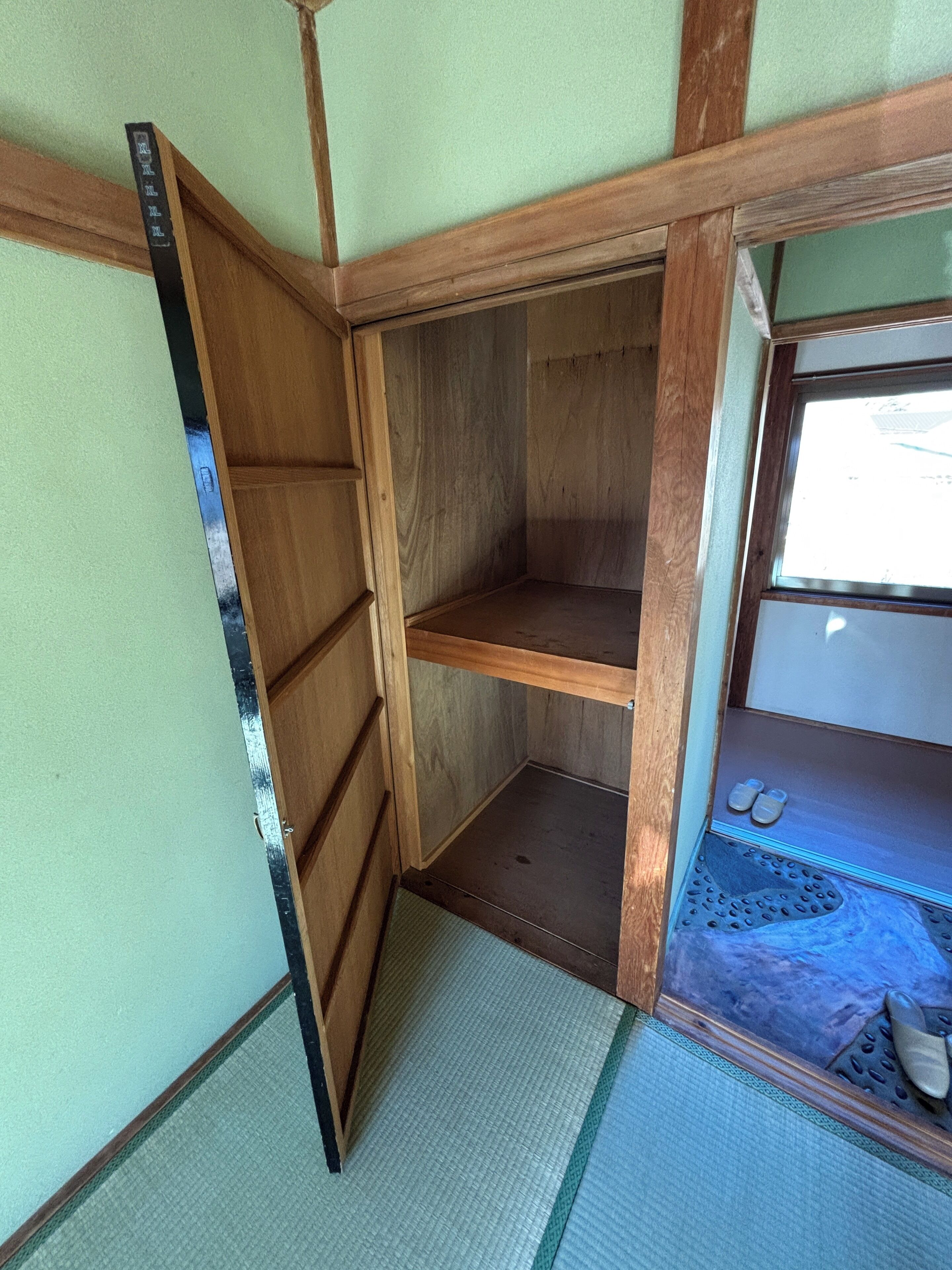 Una habitación pequeña y cerrada con suelo de madera, un ventanal y un par de zapatos en el alféizar.