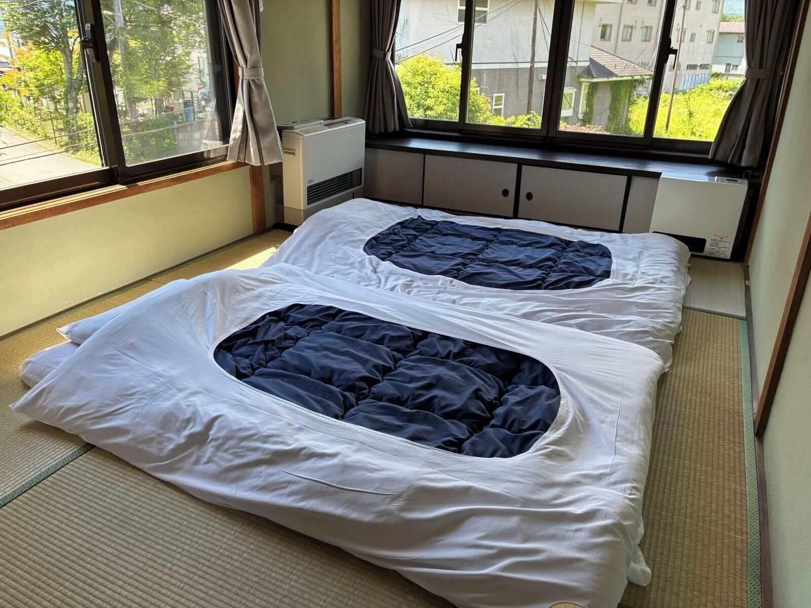 Habitación con dos camas, una ventana con cortinas, aire acondicionado y vistas a edificios.