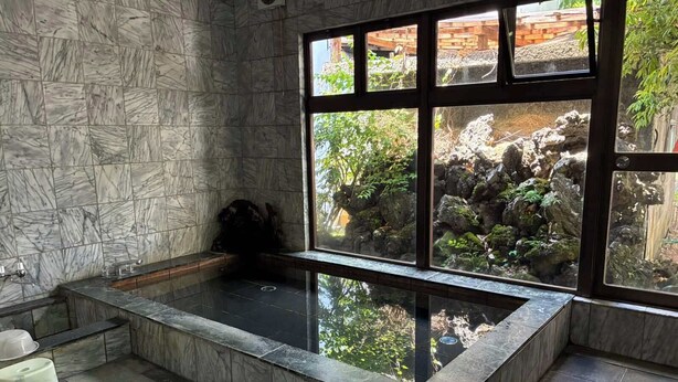 A spa room with a marble wall, a large window, and a stone bathtub.