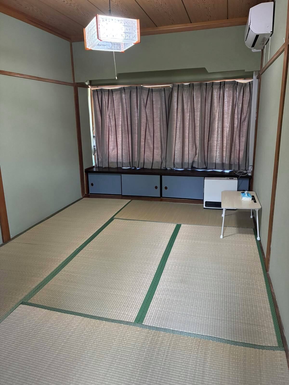 A room with tatami flooring, a futon bed, a small table, and a window with curtains.