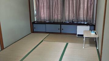 A room with tatami flooring, a futon bed, a small table, and a window with curtains.