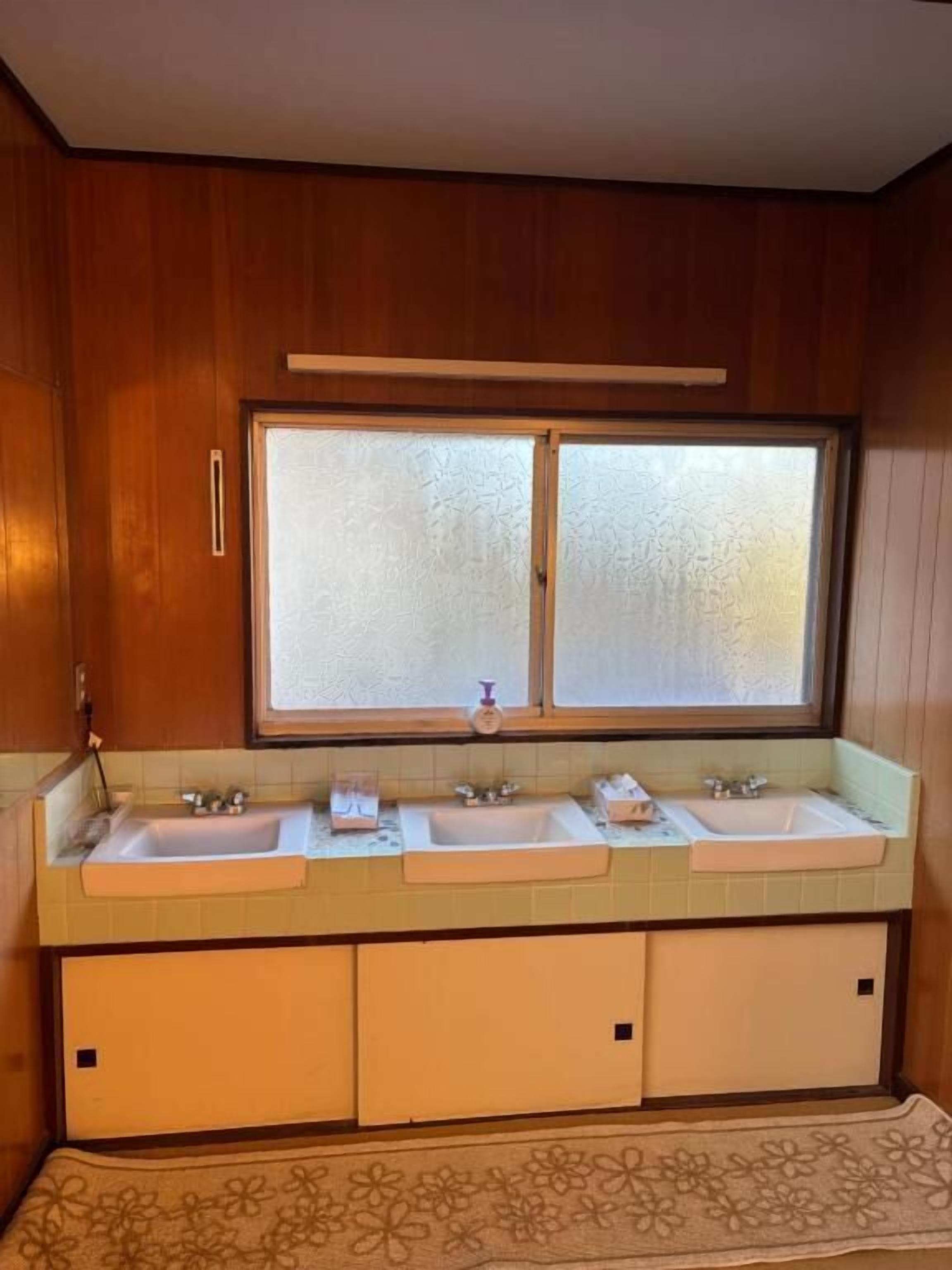 A bathroom with wooden cabinets, a large frosted window, and three sinks.