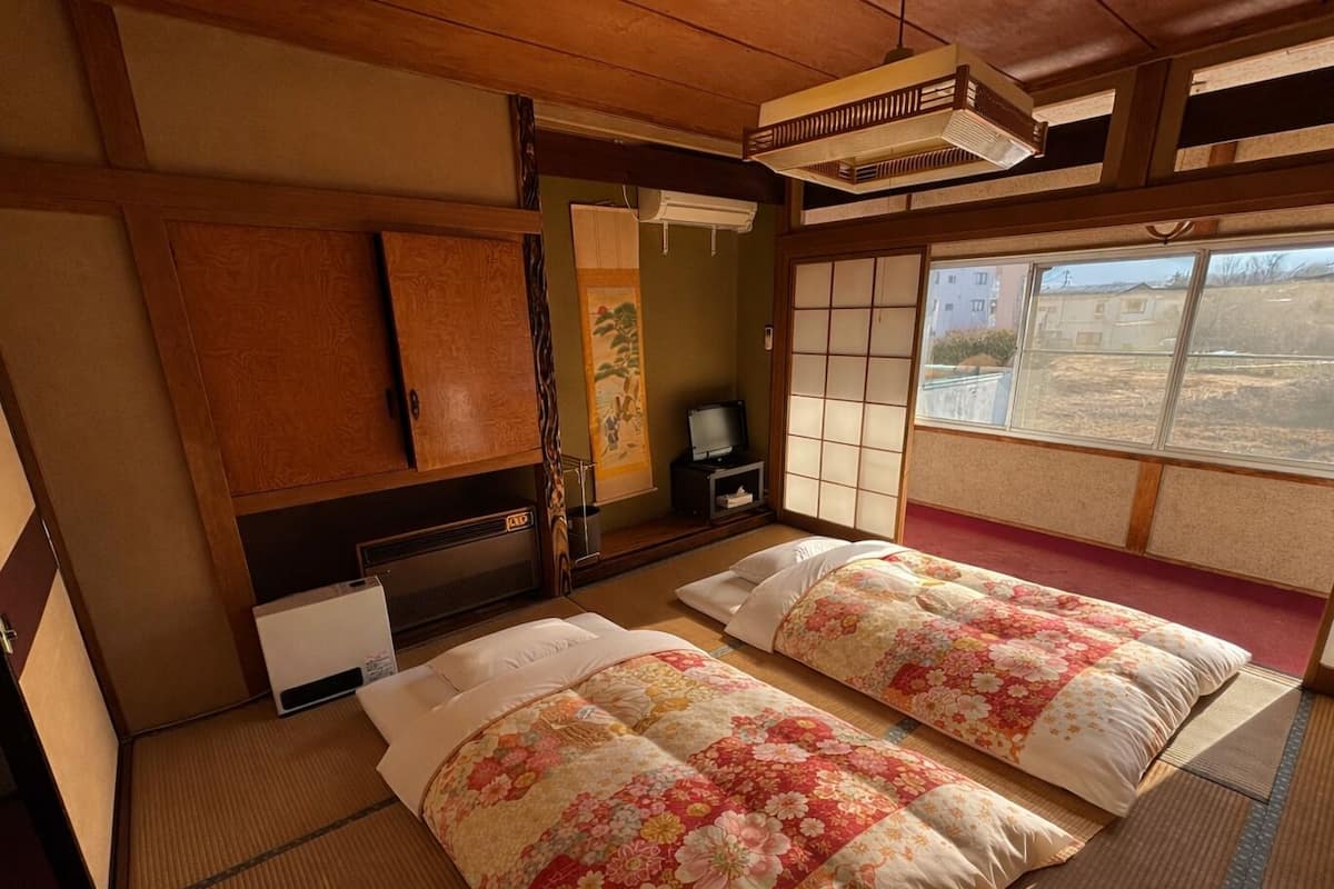 A traditional Japanese room with tatami flooring, two beds with floral bedding, a television, and a sliding shoji screen.