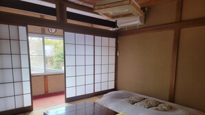 A traditional Japanese room with tatami flooring, a futon bed, a wooden table, sliding shoji doors, and a ceiling fan.