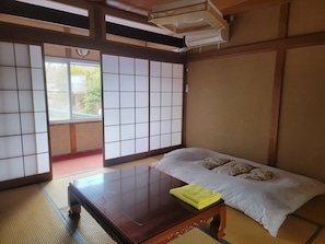 A traditional Japanese room with tatami flooring, a futon bed, a wooden table, sliding shoji doors, and a ceiling fan. - HOTEL Mt.Fuji MoMoAung (Yamanakako)