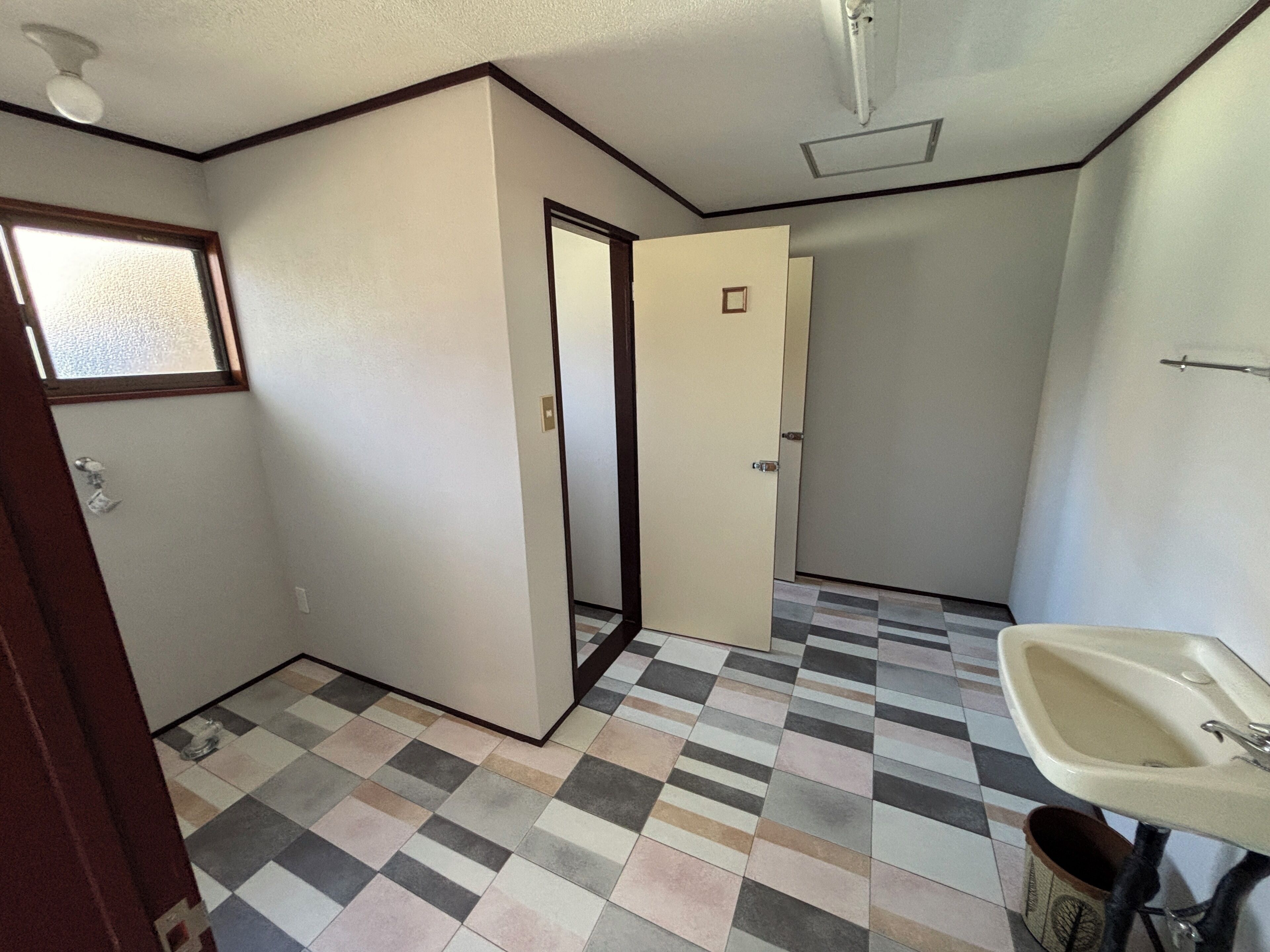 Un baño con piso a cuadros, un lavamanos y una puerta que da a otra habitación.