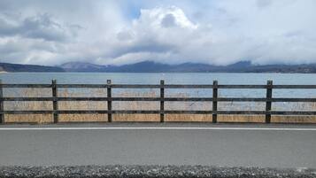 A view of a lake with mountains in the background, a wooden fence in the foreground, and a cloudy sky.