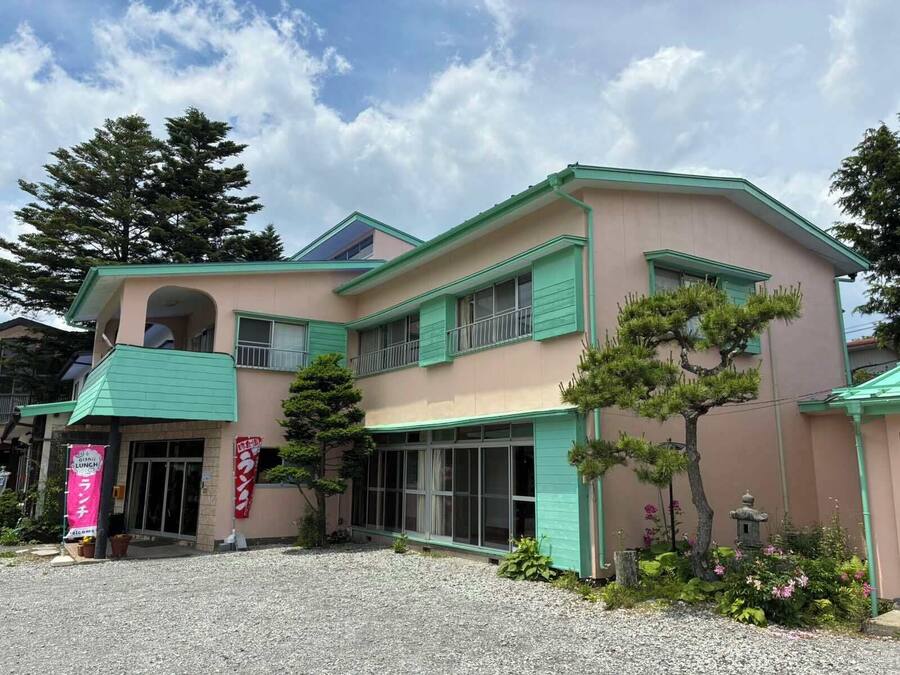 A two-story building with a green and beige facade, a balcony, and a gravel driveway.