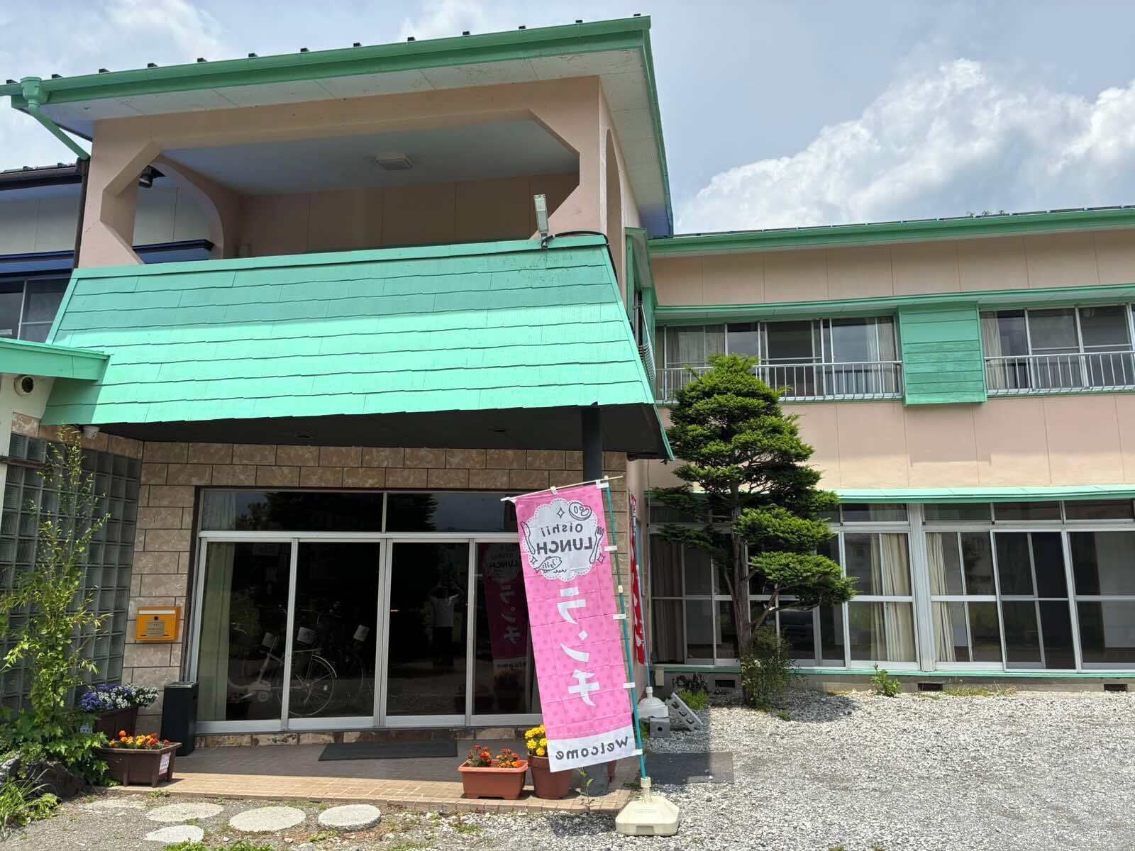 A building with a green roof, a large glass entrance, and a pink banner.