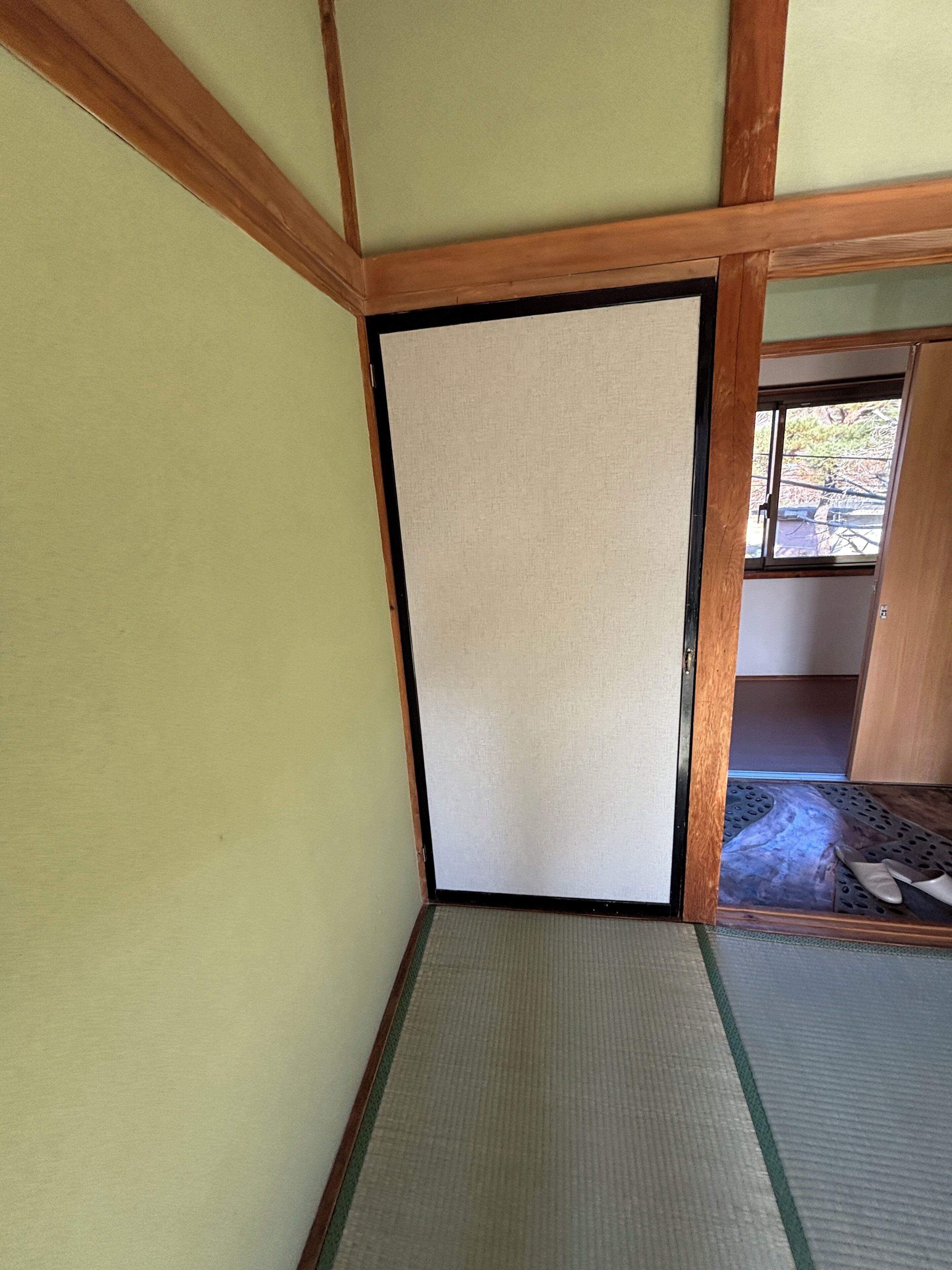 A traditional Japanese room with tatami flooring, a sliding door, and a view of the outside.