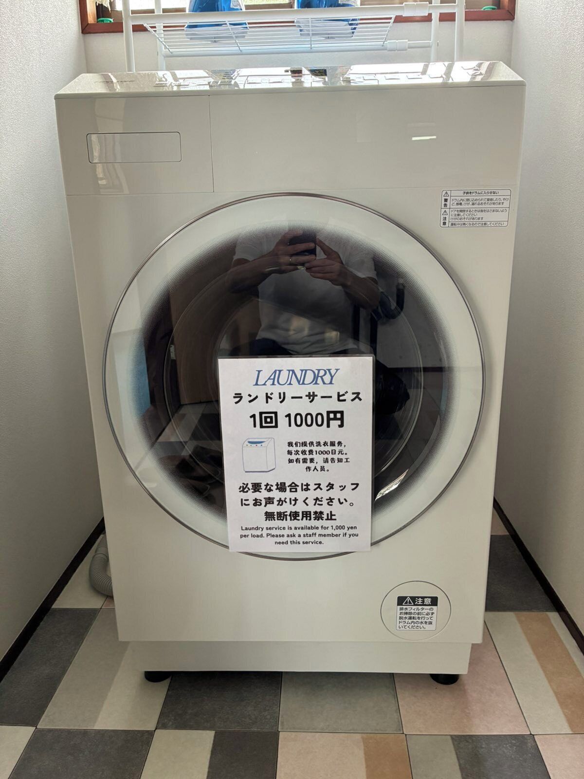 Een voorlader wasmachine met een bordje dat een wasserijservice aangeeft voor 1000 yen per was.