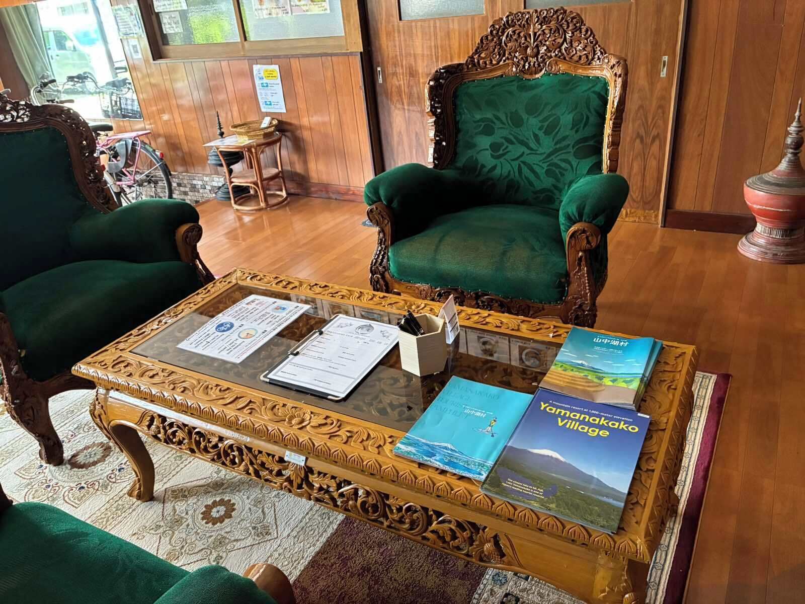 A room with two green upholstered chairs, a wooden coffee table with documents, and a book titled 'Yamanakako Village'.