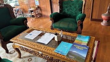 Una habitación con dos sillones tapizados en verde, una mesa de centro de madera con documentos y un libro titulado 'Yamanakako Village'.