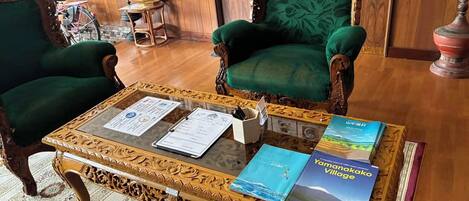 A room with two green upholstered chairs, a wooden coffee table with documents, and a book titled 'Yamanakako Village'.