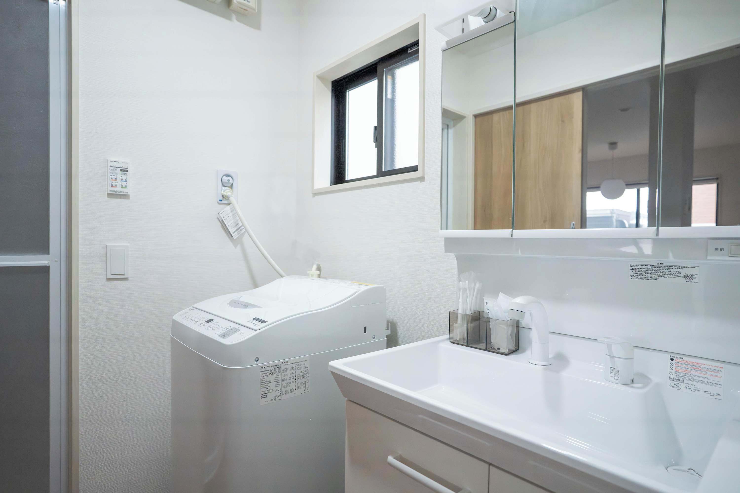 A modern bathroom with a white sink, a mirror, a window, and a wall-mounted heater.