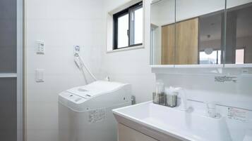 A modern bathroom with a white sink, a mirror, a window, and a wall-mounted heater.