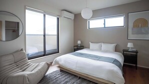 A bedroom with a bed, a sofa, a large window, an air conditioning unit, a lamp, and a framed picture on the wall. - Bright 4BR Home in Ozu Sleeps 11 by Restavio (Ozu Town, Kikuchi District)