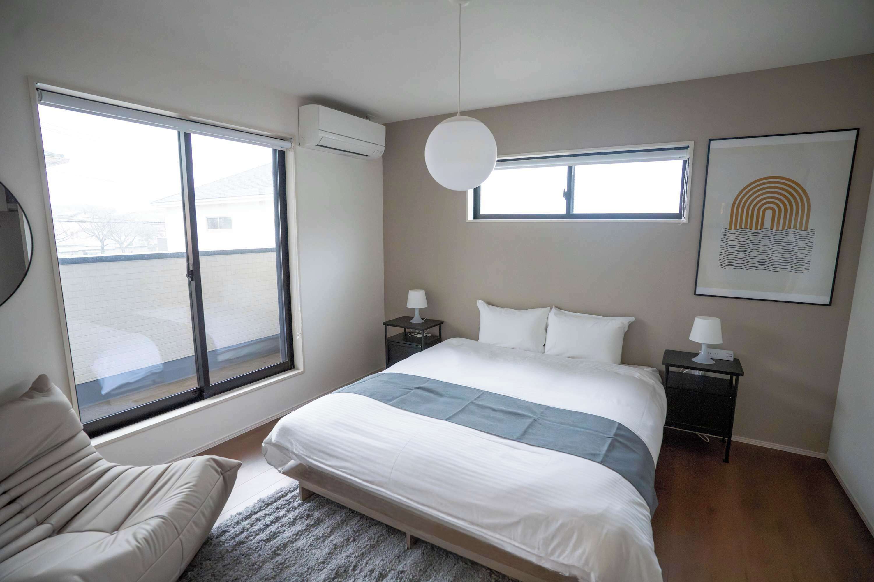 Un dormitorio con cama, sofá, ventana, aire acondicionado montado en la pared, luz de techo e imagen enmarcada.