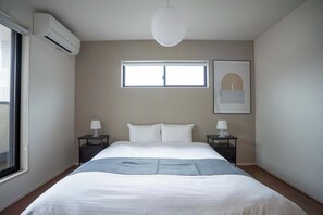 A hotel room with a bed, two bedside tables, a window, an air conditioning unit, and a hanging light fixture.