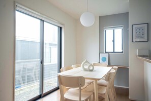 A dining area with a table and chairs, a pendant light, and a view through a sliding glass door.