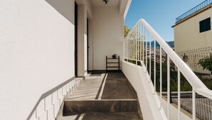 Uma escadaria leva a uma varanda com guarda-corrimão branco, uma porta e uma pequena prateleira.