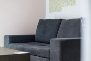 A grey sofa in a room with a wooden table and a wall with a textured pattern. - GuestReady - Cosy Apartment in vibrant Funchal (Funchal)