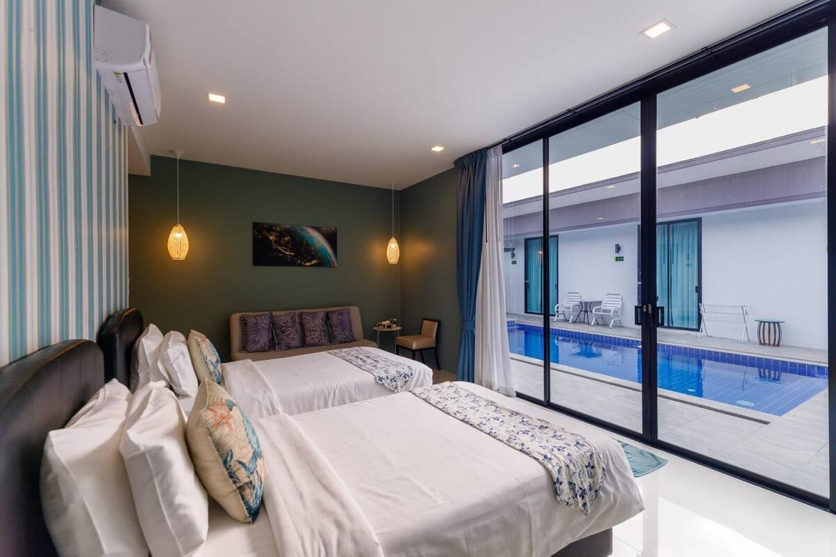 Habitación de hotel con dos camas, un ventanal grande, un equipo de aire acondicionado, un cuadro y vista a una piscina al aire libre.
